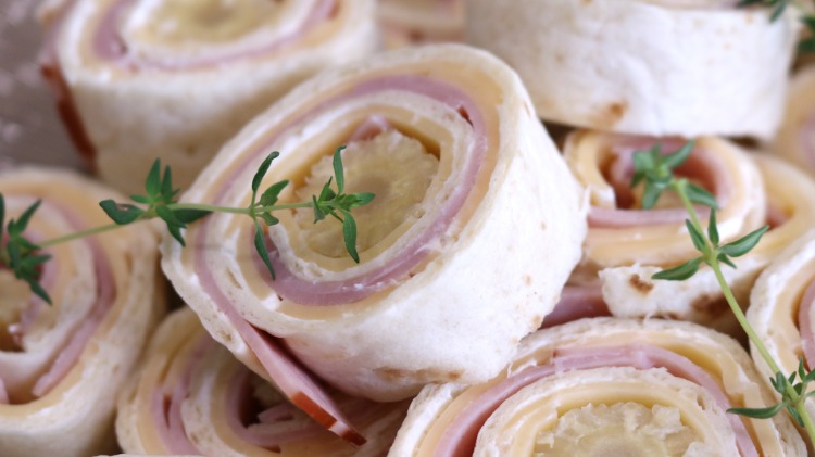 fingerfood häppchen aus gerollten tortilla wraps mit schinken und käse dekoriert mit petersilie oder kresse