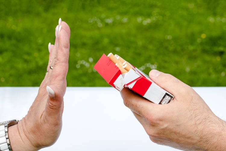 weibliche arm macht eine anhaltende geste richtung zigarettenschachtel im freien