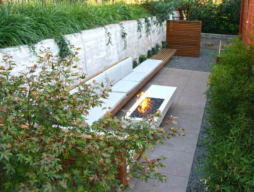 Hohe Mauer aus Beton im Garten entlang eines Sitzbereichs mit Feuerstelle