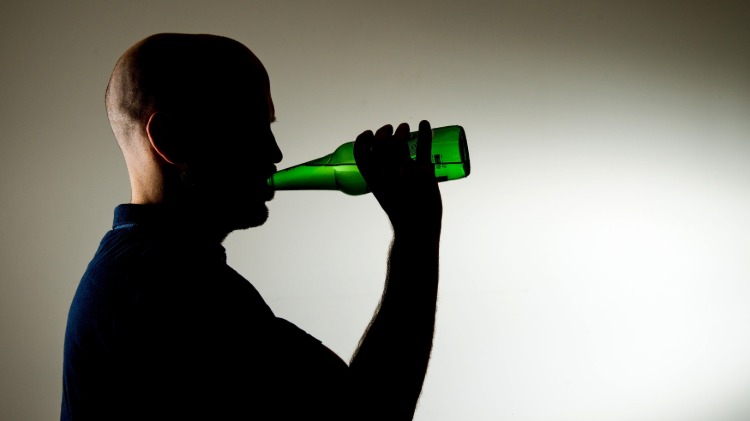 alkoholkonsum reduzieren mann trinkt aus einer bierflasche im dunklen