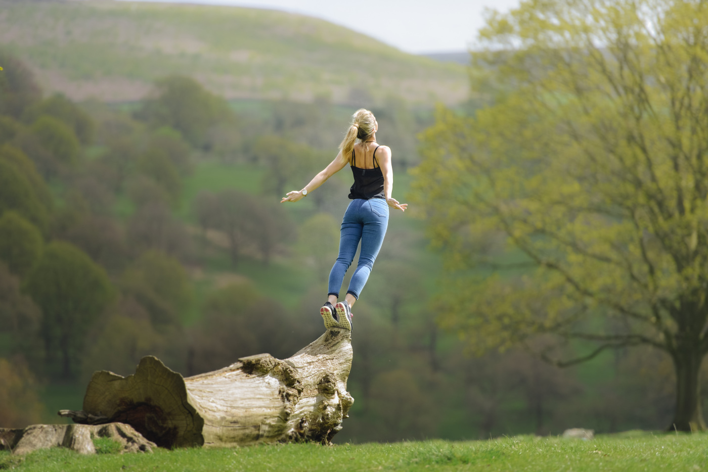 blonde frau mit jeans steht auf einem baum und verucht zu springen