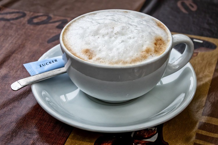 cappuccino mit schaum in weißer tasse mit unterteller und zucker