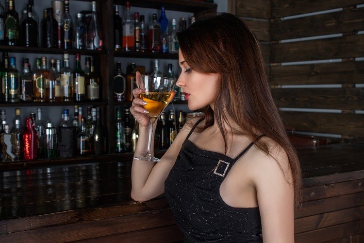 junge frau in einer bar hält ein halbvolles weinglas vor aneren alkoholflaschen