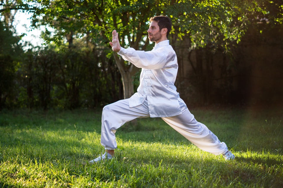 mann mit weißem tai chi anzug übt kampfkunst im wald aus