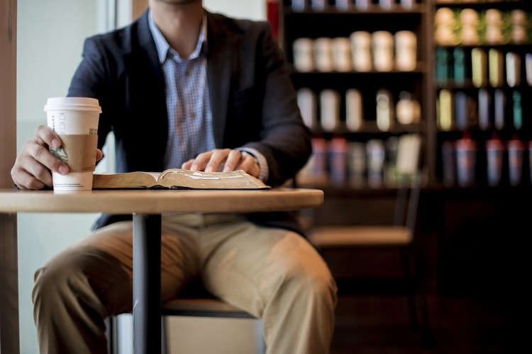mann sitzt im cafe mit büchern im hintergrund und liest buch