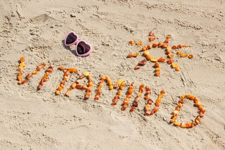 mit steinen auf dem sand geschriebene aufschrift von vitamin-d und sonne