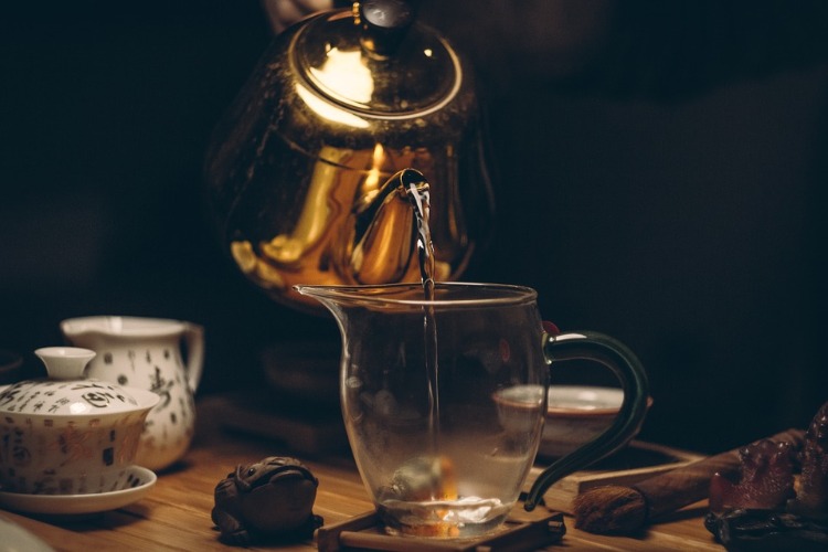 schwarzer tee mit koffei aus silberner kann in glas gießen
