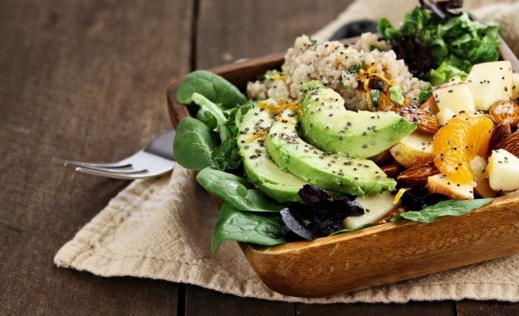 vegetarisches gericht mit avocado quinoa äpfeln mandarinen und spinat in schüssel aus holz