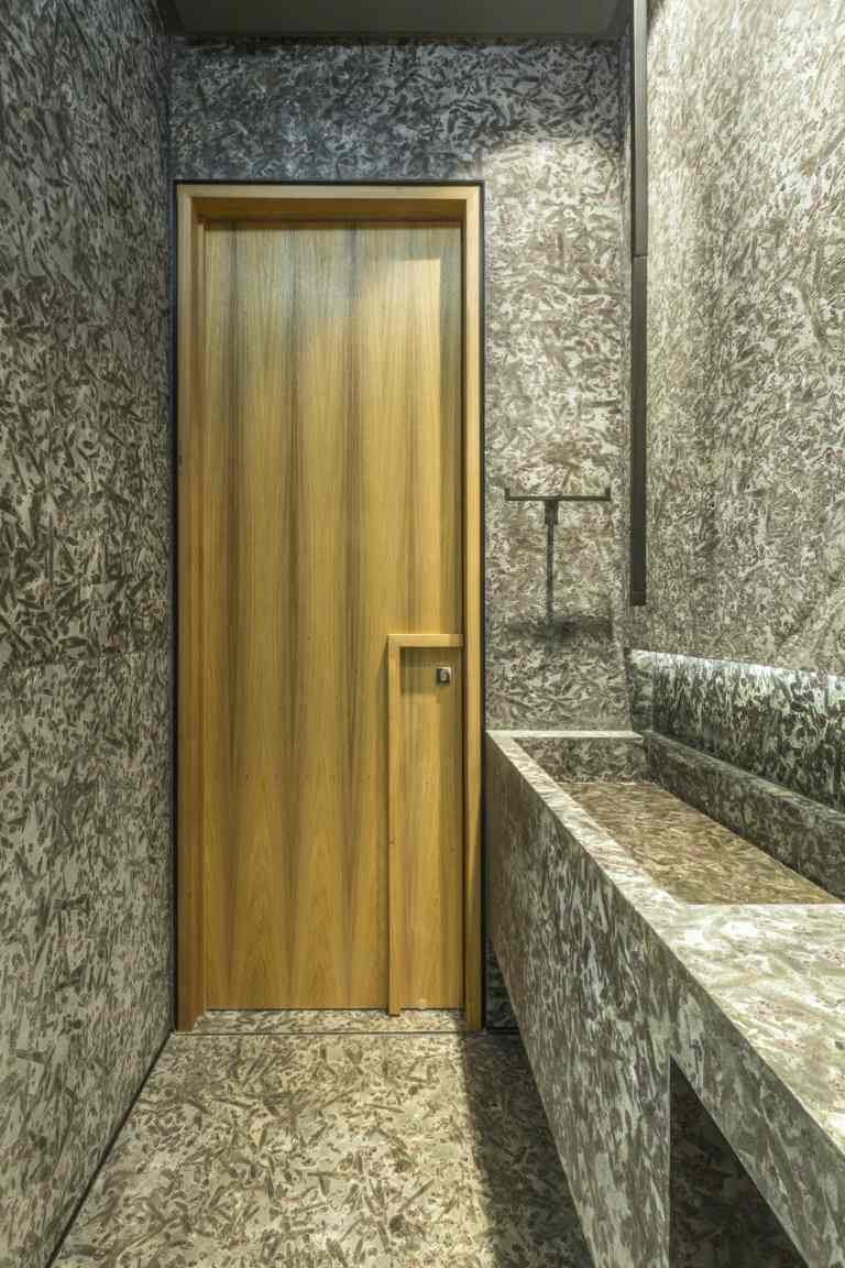 Graue Badgestaltung mit Holztür als farblicher Akzent und eingebautes Waschbecken