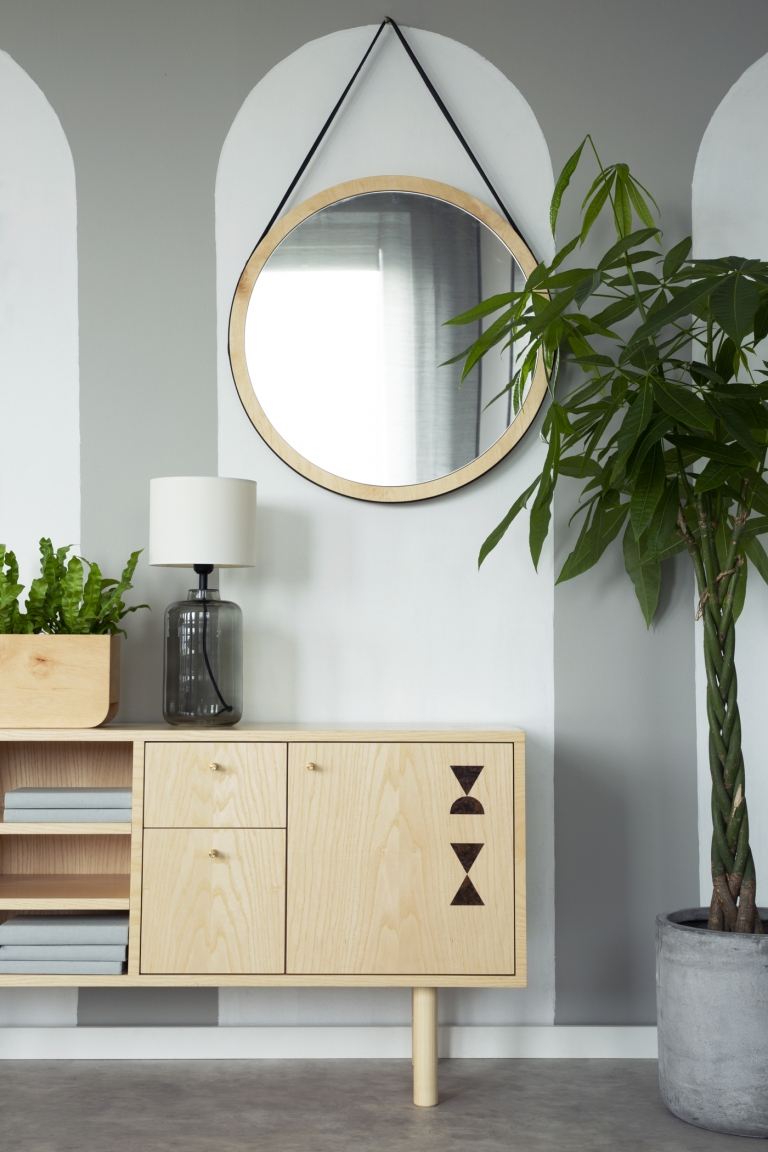 Kommode aus hellem Holz runder Wandspiegel und Zimmerpflanze