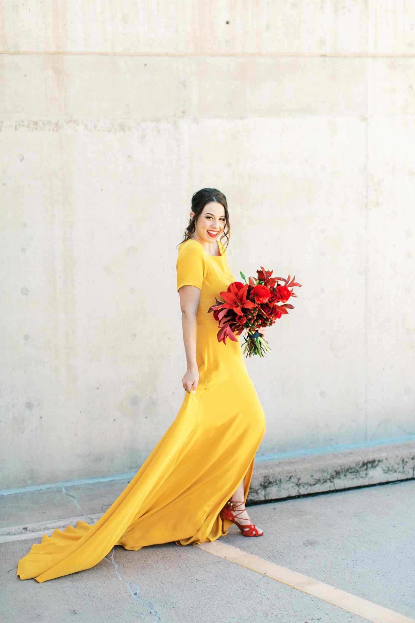 Originelles, gelbes Brautkleid mit Schleppe und Ärmeln, roten Schuhen und rotem Brautstrauß