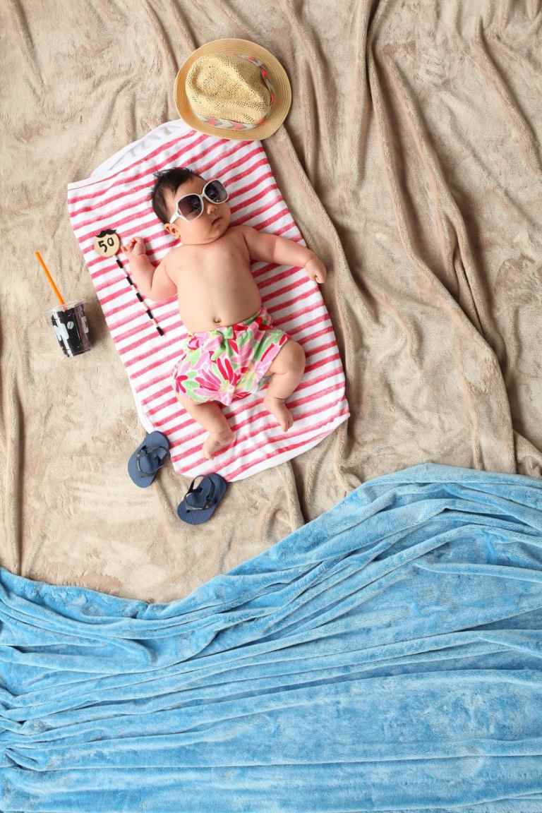 baby auf decke für den strand mit sonnenbrille getränk und flip flops