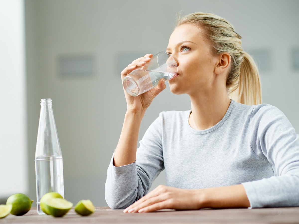 blonde frau trinkt wasser aus glas wegen täglicher wasseraufnahme besserung