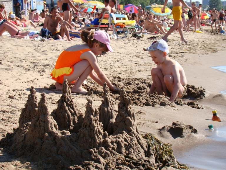 zwei kleine kinder bauen sandburgen am strand voll mit menschen