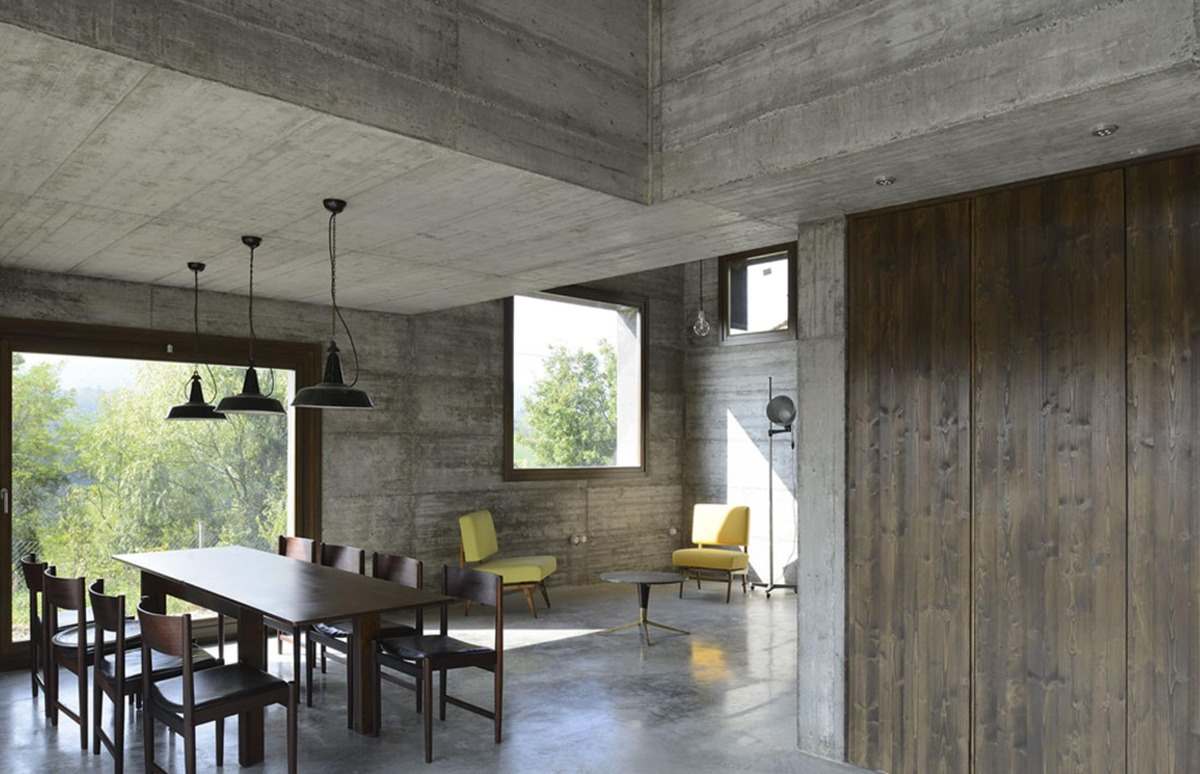 großer offener wohnraum mit esstisch aus holz gelben stühlen im betonhaus