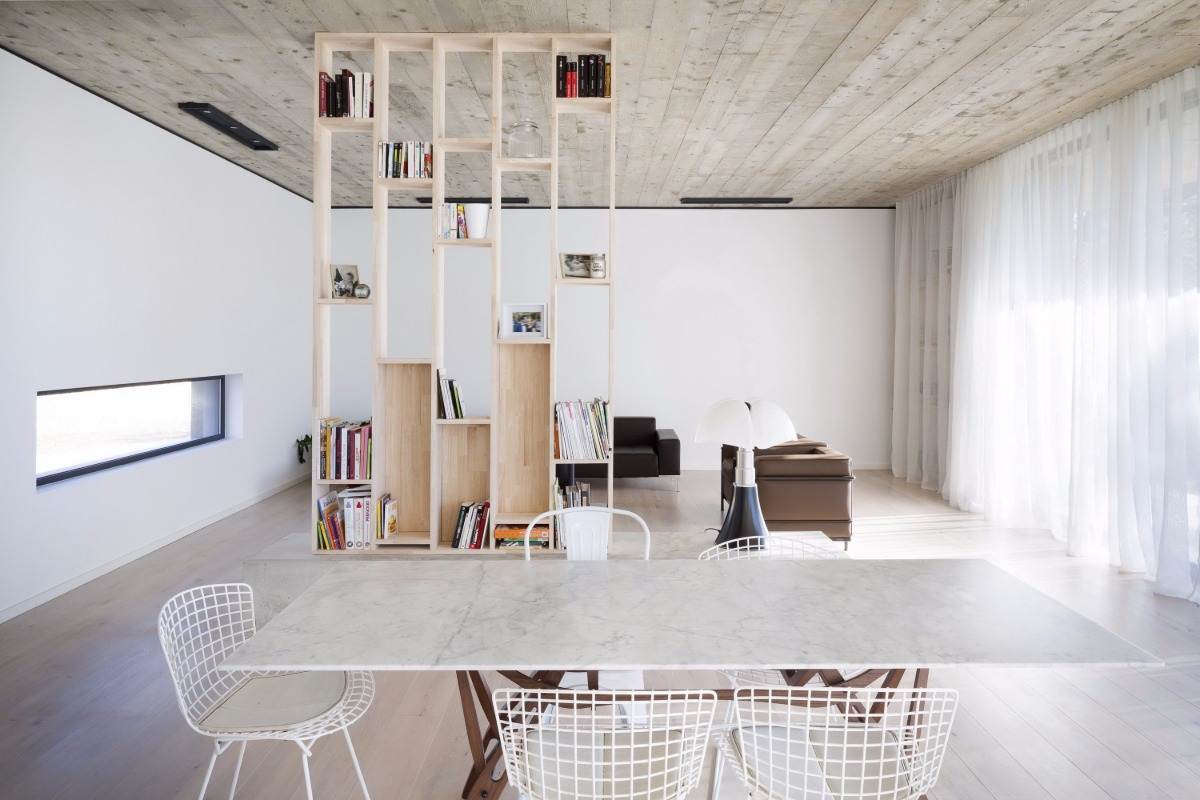 innenraum von maison 0 82 mit bücherregal aus holz marmortisch betondecke und großen fenstern