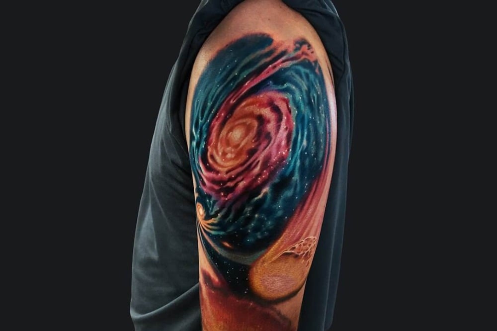 kosmos galaxie tattoo schulter mann farbig mitdunklem hintergrund
