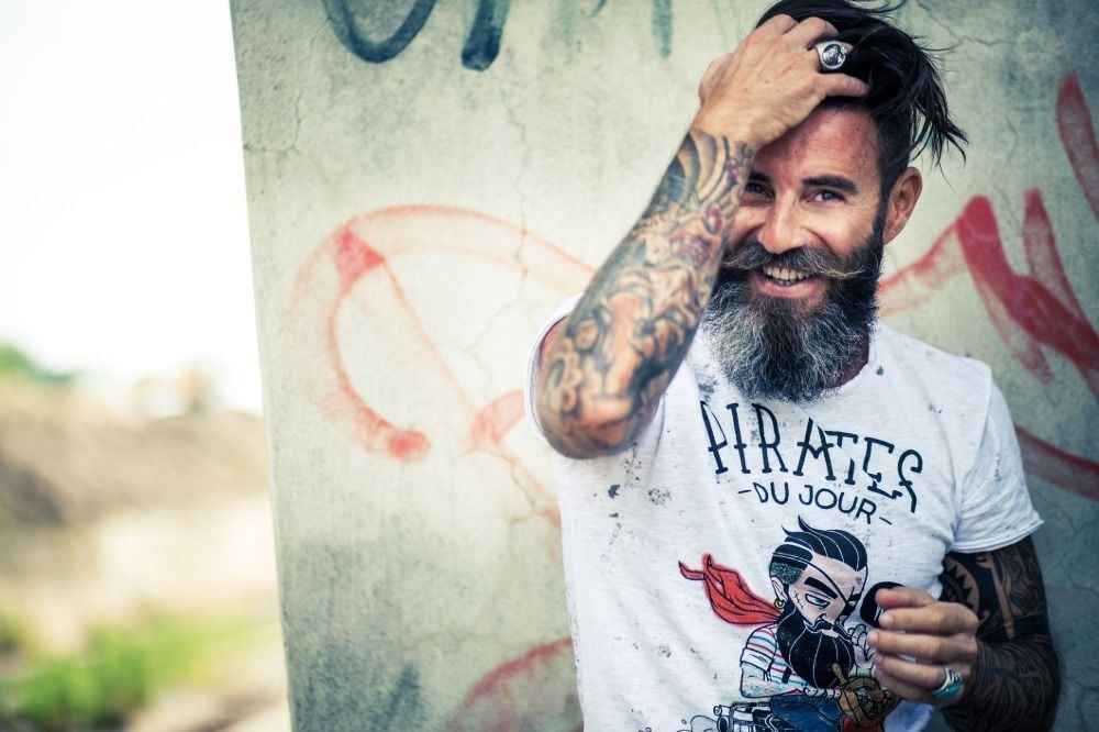 lachender mann mit bart und moderner frisur zeigt seine arm tattoos männer