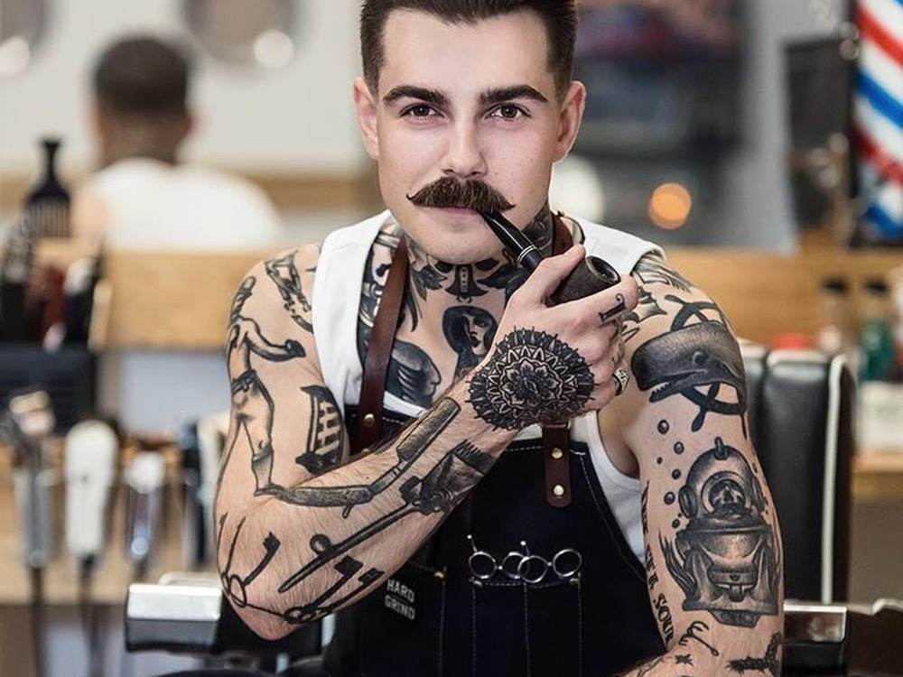 tattoo arm mann mit schnurbart und pfeife posiert mit seinen kunstwerken am körper