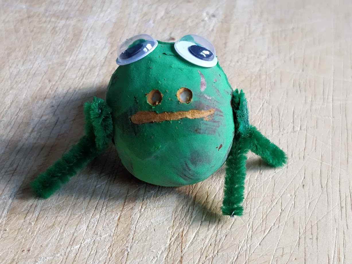 Grün bemalter Frosch mit Augen und Mund einfachen Beinen aus Plüschdraht