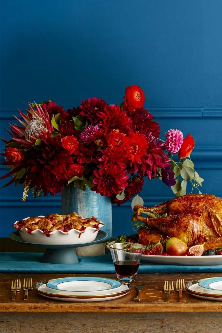 Herbstdeko in Rot Blumengesteck mit Dahlien und Rosen und Ranunkel in himmelblauer Vase am Tisch