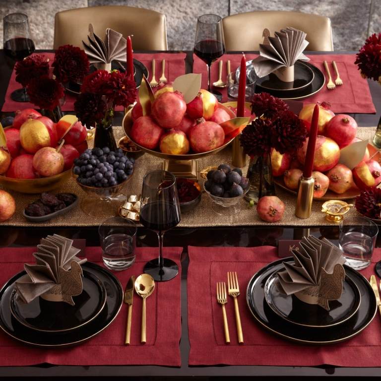Herbstliche Tischdeko mit weinroten Dahlien und in gold bemalten Früchten und Weintrauben und schön gefalteten Servietten