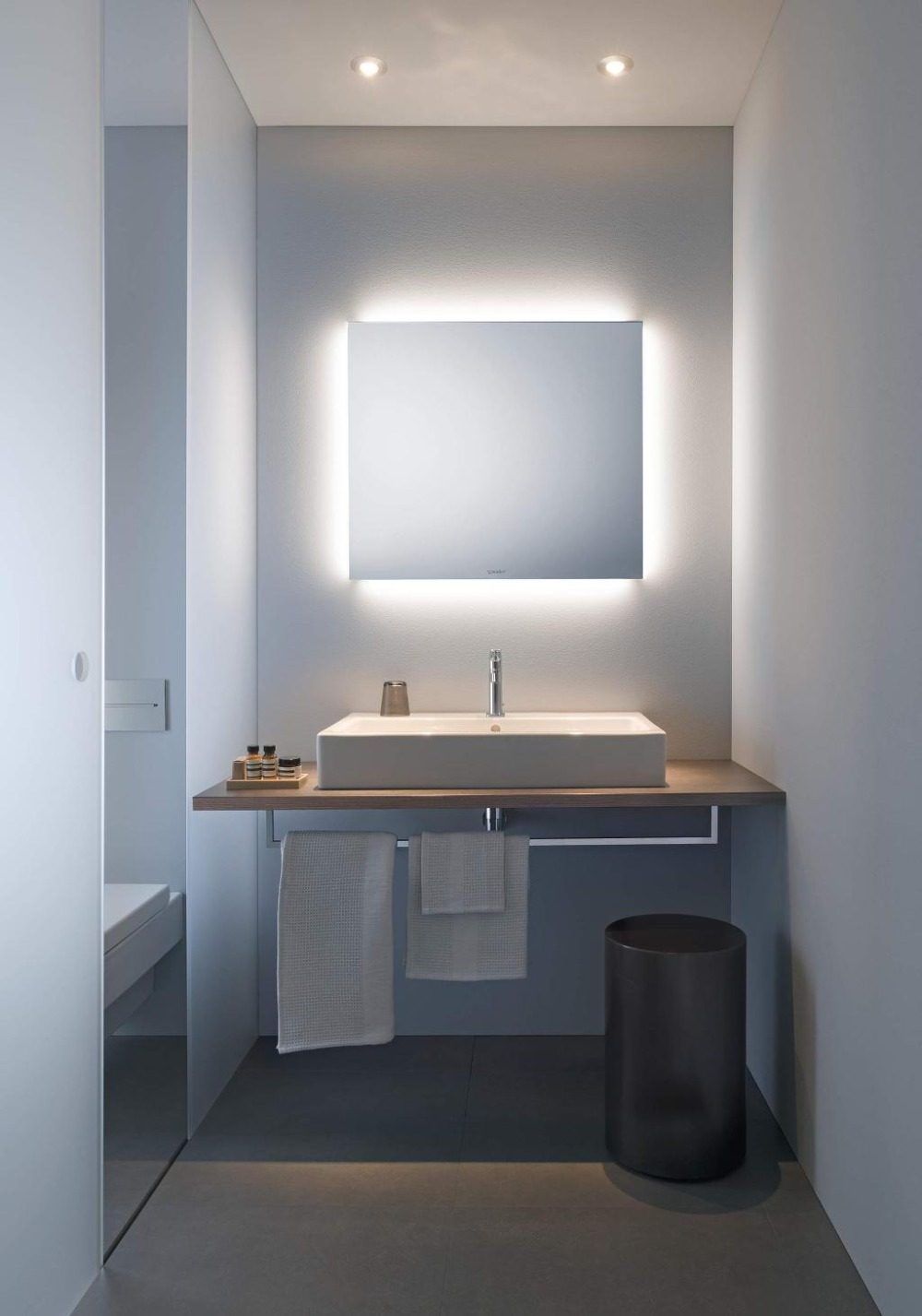 enger badraum mit waschtisch und quadratischem spiegel indirekt beleuchtet