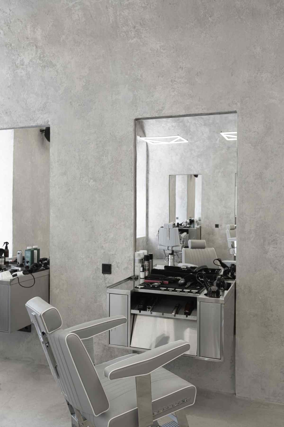 großer spiegel im friseursalon mit drehstuhl aus grauem leder und dekorputz wandverkleidung