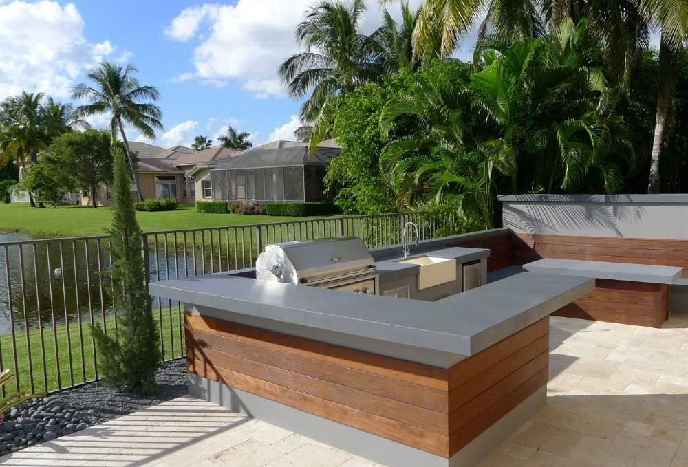 ultra modern l-shaped outdoor kitchen made of stainless steel and wood in sunny garden