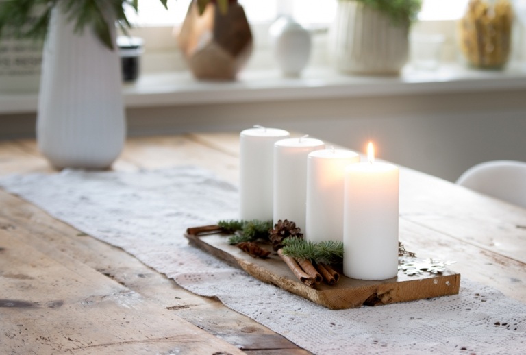 Weihnachtsgestecke auf Holzschale Zimtstangen und Tannenzweige und Tannenzapfen mit weißen Kerzen