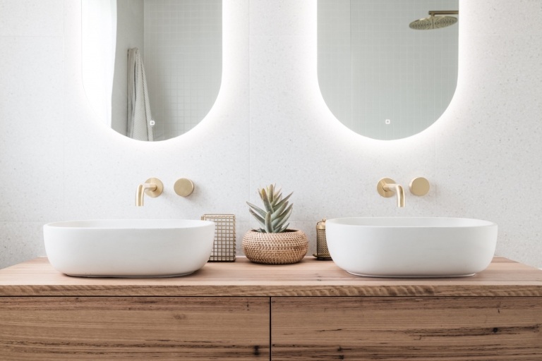 Moderne Bäder mit Holz Waschtisch Unterschrank und Aufsatzbecken und Badarmaturen in Goldoptik und Spiegel mit Beleuchtung und weiße Granitfliesen