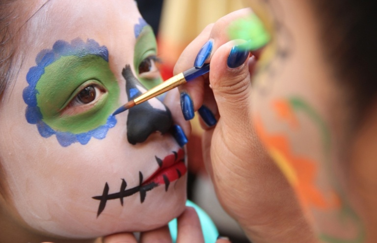 Halloween Make-up Mädchen mit Gesichtschminke Blüten malen mit flüssiger Gesichtsfarbe