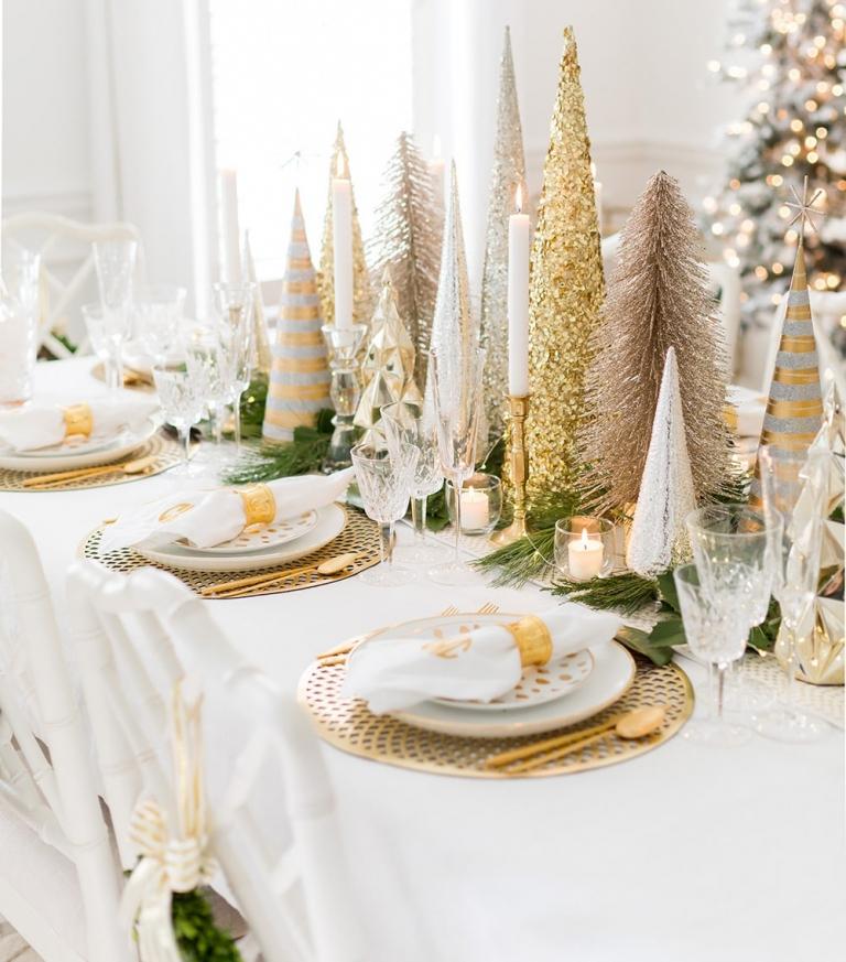 Weihnachtsdeko Tisch decken mit Windlichtern mit Duftkerzen und künstliche Weihnachtsbäume und Zypressenzweigen und goldenem Besteck