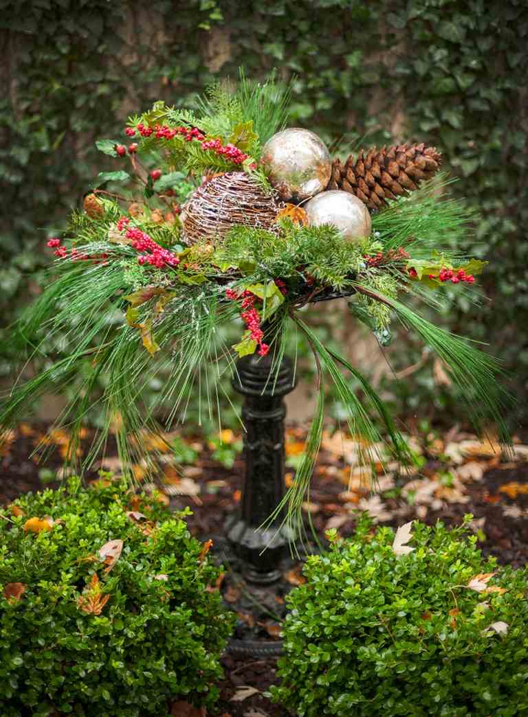 Winterdeko Garten Tannengrün Beeren Holzkugel und goldene Christbaumkugeln und Tannenzapfen im Garten arrangieren