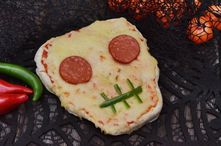 Witzige Halloween Pizza in Form eines Totenkopfs mit Salami, Paprika und Käse