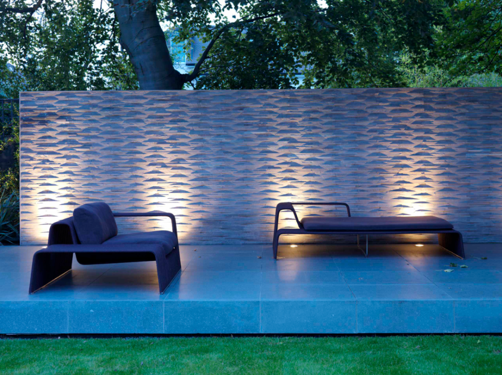 this stone wall illumination outside a pool with chairs in the garden area