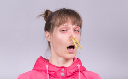 frau mit rosafarbener jacke und gelber wäscheklammer an der nase verstopft