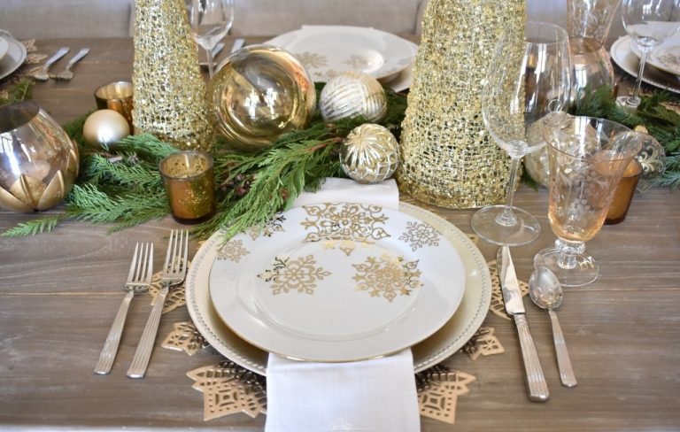 gedeckter Tisch zu Weihnachten mit Zypressenzweigen und Goldkugeln und Windlichtern