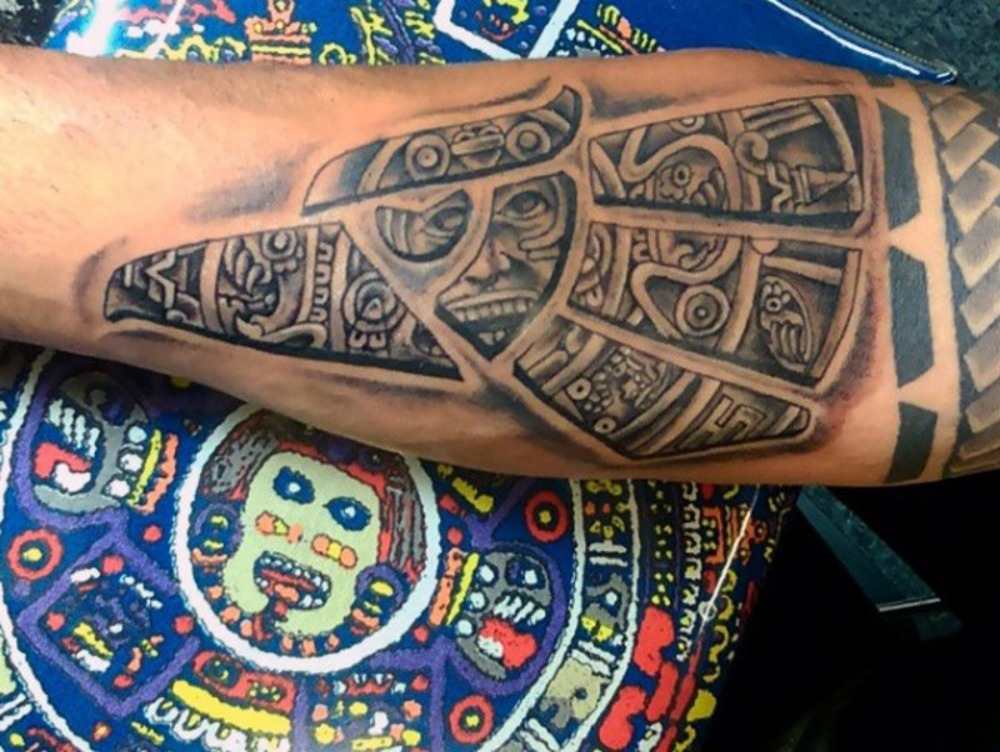 innenseite von unterarm tätowiert mit aztekischen symbolen auf farbiger unterlage