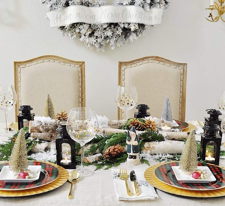 pfestlich gedeckter Weihnachtstisch mit Porzellan-Dekofiguren und Baumstamm und Tannenzapfen und Kunstschnee