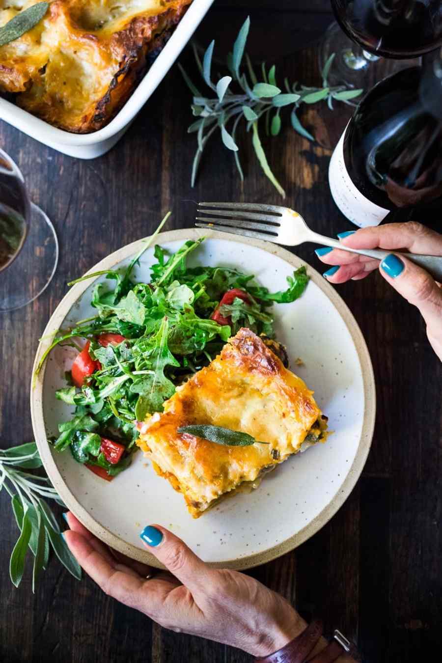 servieren von butternut kürbis lasagne in teller mit rucola salat und salbei