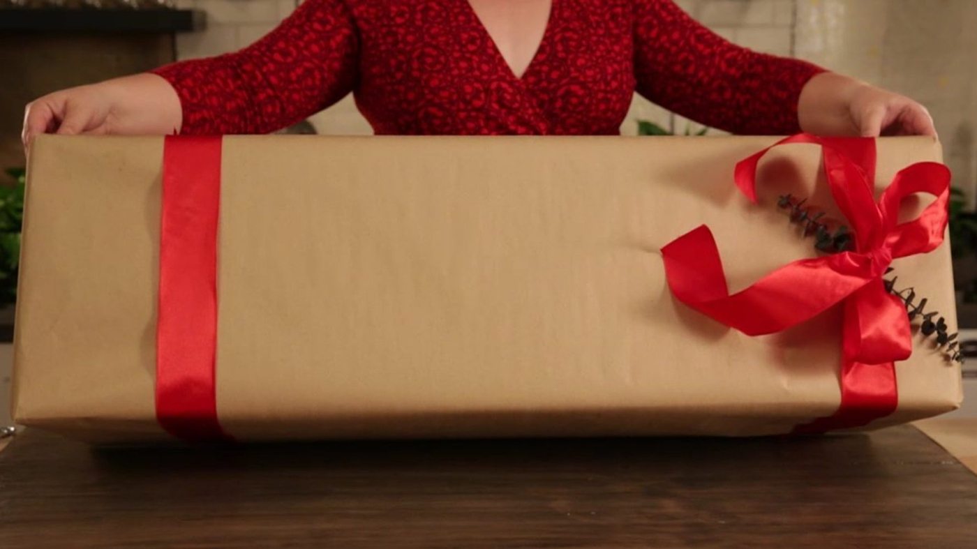 Große Geschenke verpacken mit Geschenkpapier und hübschem Band in roter Farbe