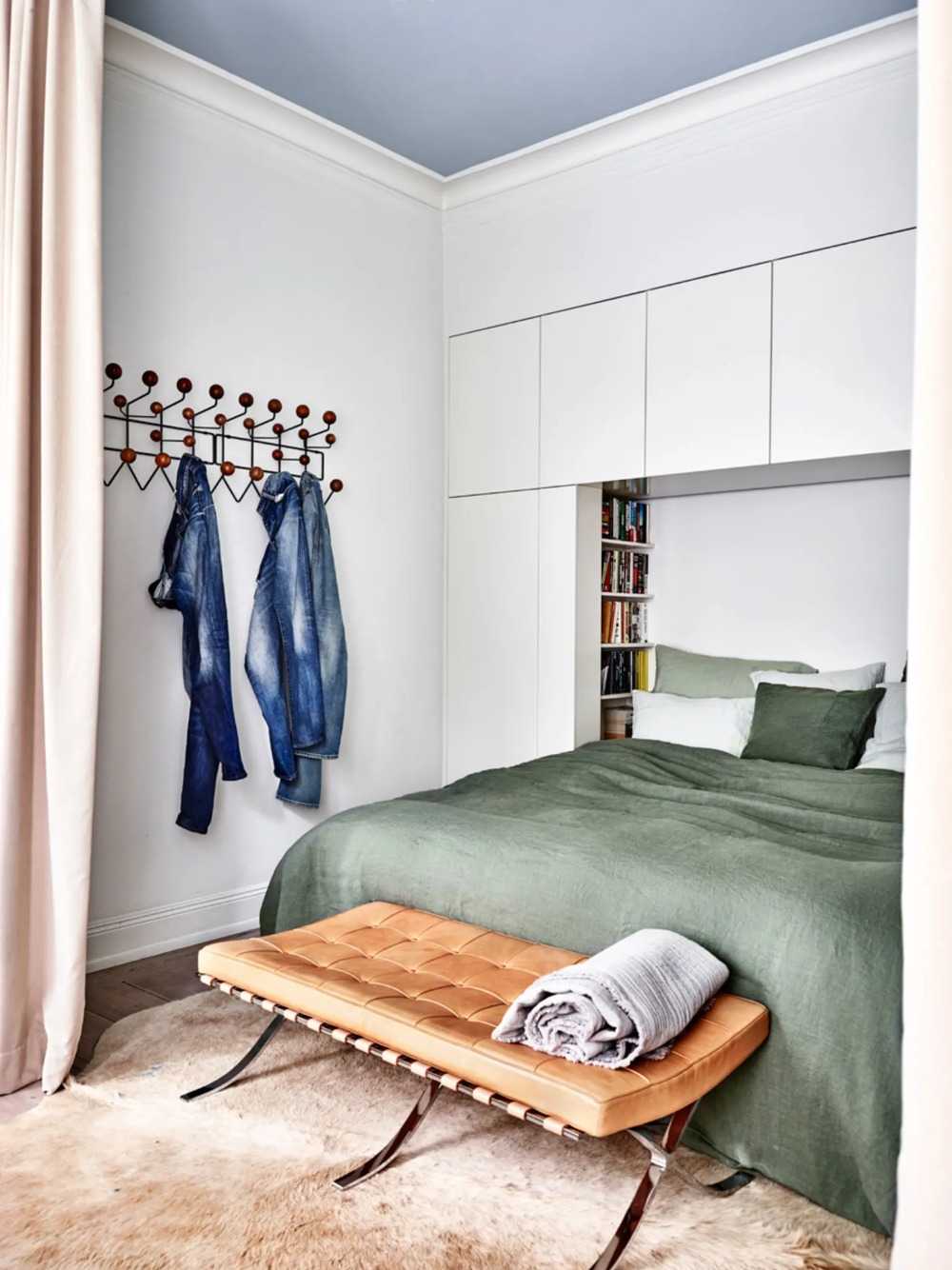 schlafzimmer heller boden mit rindshaut und ottomane mit leder neben grünen bettbezügen