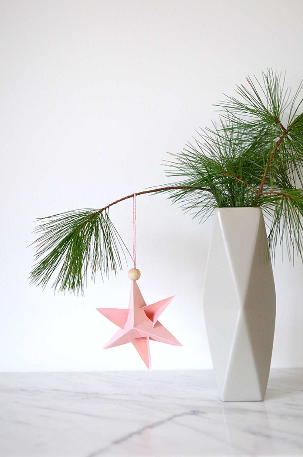 schön gestaltete weihnachtsdeko mit baumzweigen in vase dekoriert mit papierstern hängend mit holzperle