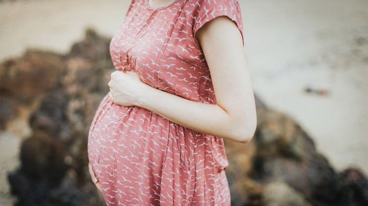 schwangere frau mit rotem kleid hält ihren bauch stehend an felsen