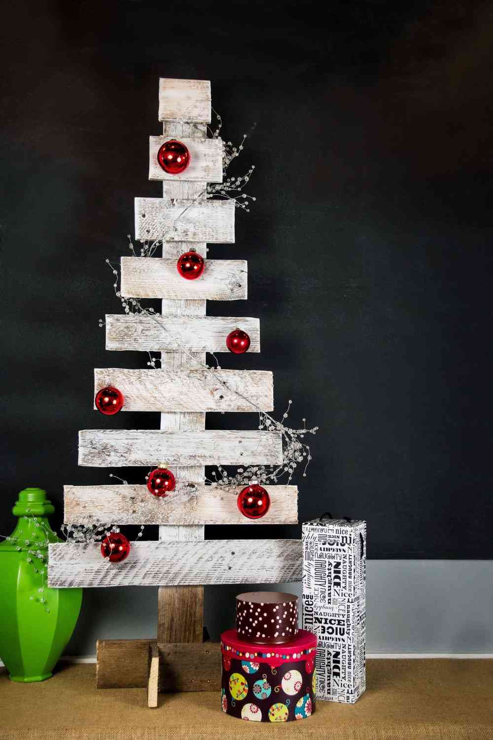 weißer paletten weihnachtsbaum mit roten weihnachtskugeln und weihnachtsgeschenken dekoriert