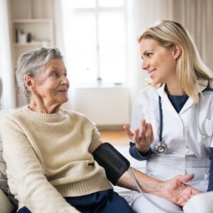 Pflegefachfrau spricht mit Frau bei Blutdruckmessung