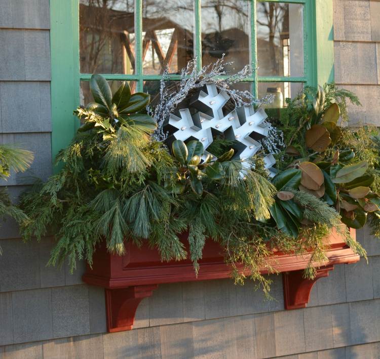 Weihnachtsdeko Fensterbank aussen Tannenzweige und Herbstblätter und beleuchtete Schneeflöcke aus Metall im Blumenkasten arrangieren