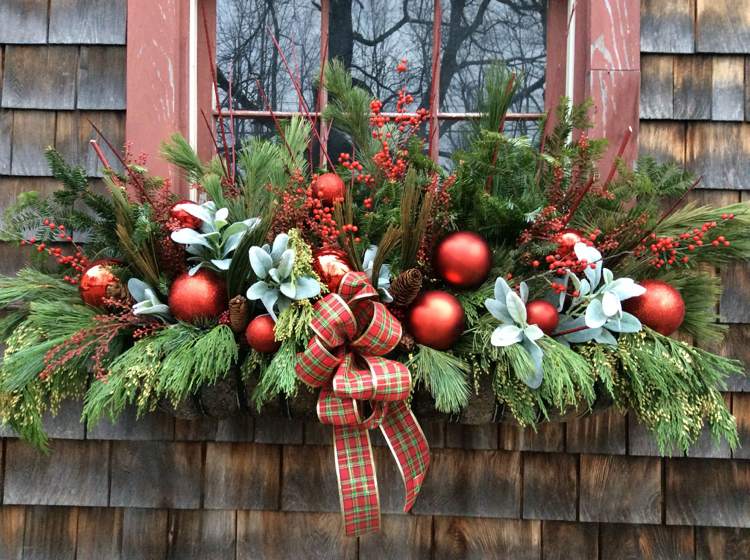 Weihnachtsdeko Ideen für Fensterbank aussen rote Weihnachtskugeln und rote Karo-Schleife und Tannengrün und Beeren und Zypressenzweige im Blumenkasten arrangieren