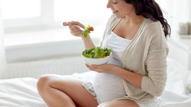 schwangere frau isst salat im bett